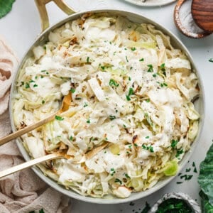 Overhead view of a skillet with alfredo cabbage ribbons with kitchen tongs.