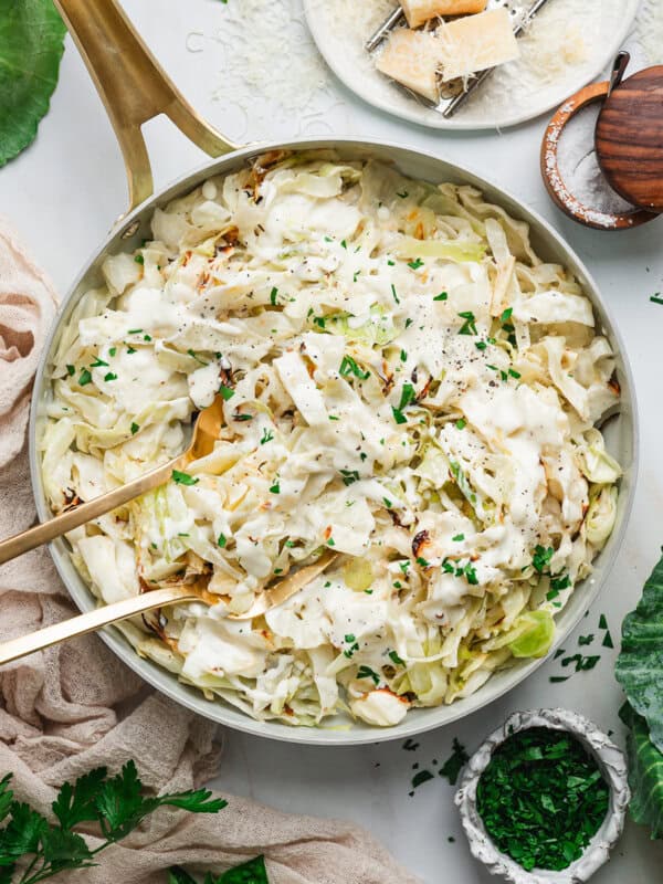 Overhead view of a skillet with alfredo cabbage ribbons with kitchen tongs.