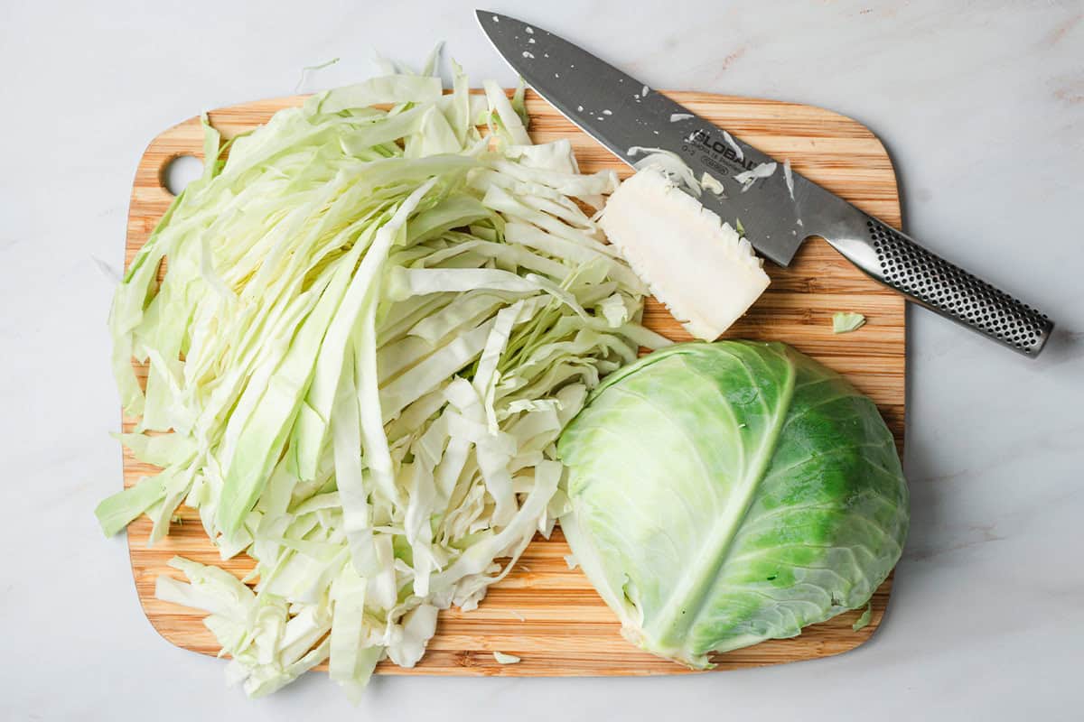A cabbage on a cutting board with half cut into thin ribbons.