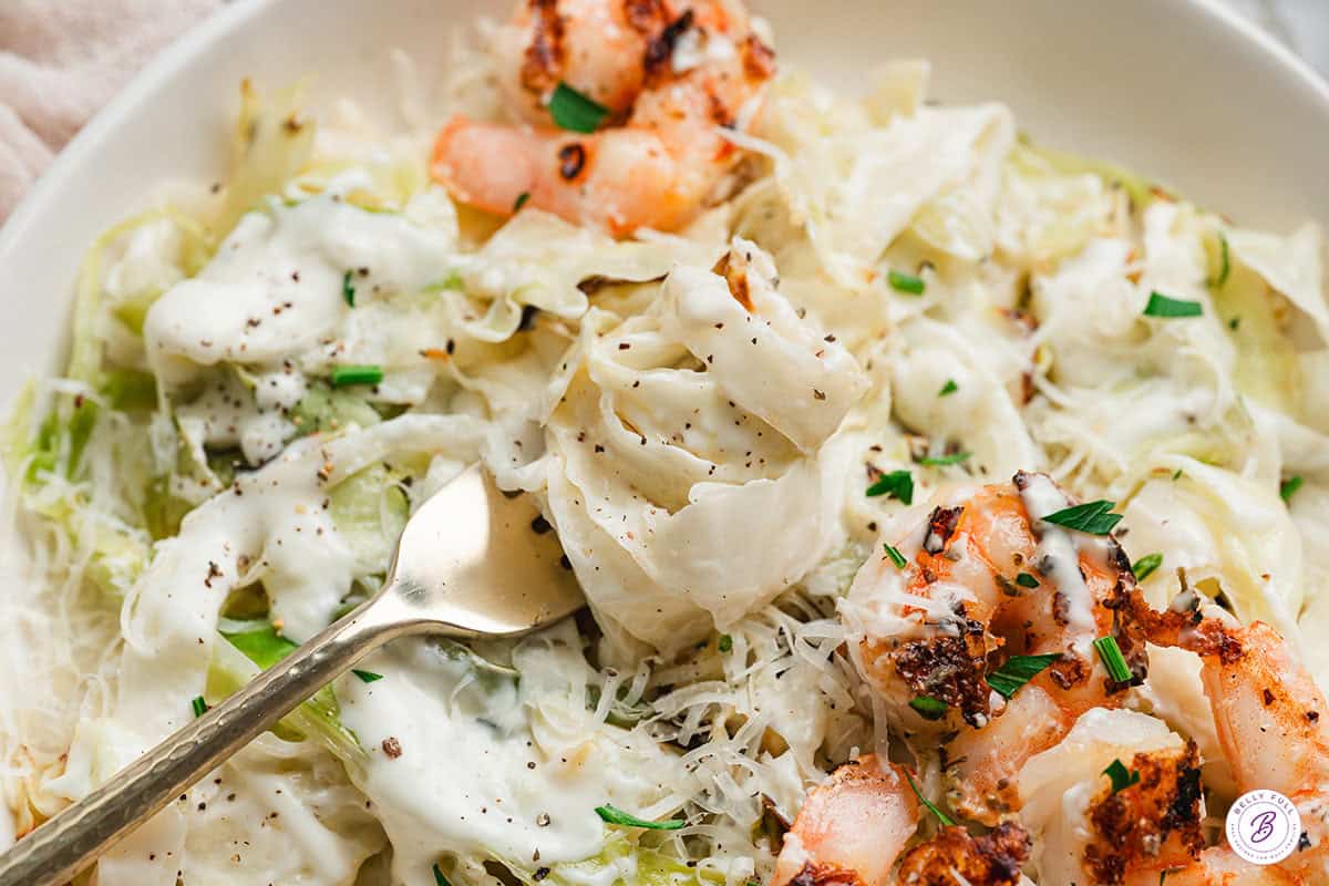 Overhead close up of alfredo cabbage ribbons on a fork with shrimp.