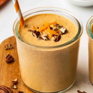 Carrot cake smoothie in a glass topped with shredded carrot and chopped pecans, with a striped straw