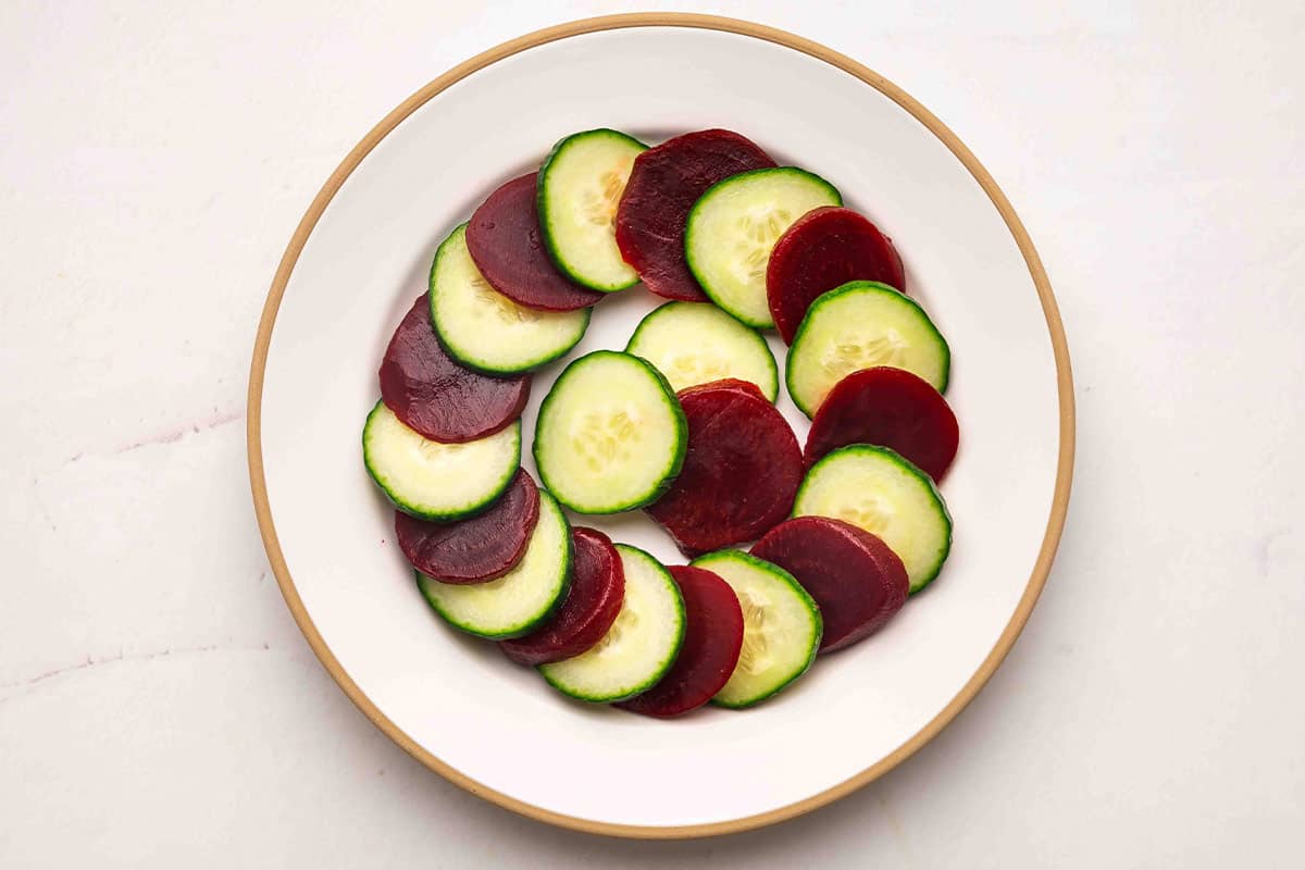 overhead cucumber and beet slices arranged in a spiral pattern on a white plate
