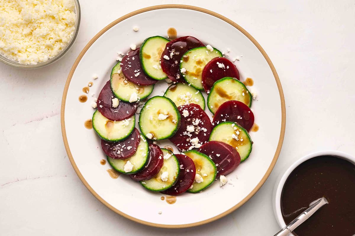 overhead cucumber beet salad drizzled with balsamic dressing and crumbled feta, dressing bowl on the side