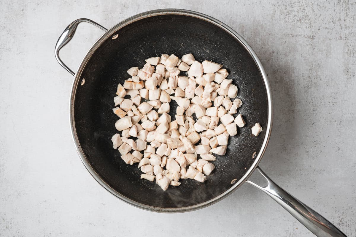 Diced chicken breast searing in a dark wok, browning in a single layer before the vegetables are added.