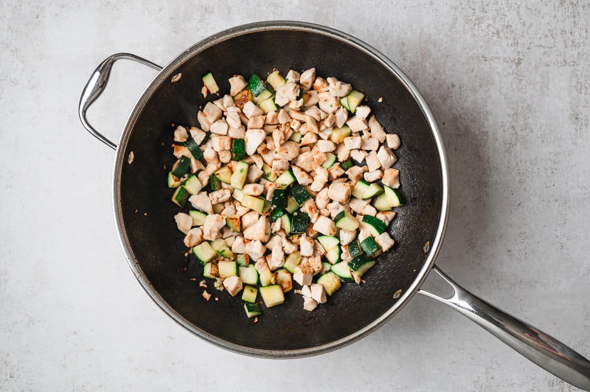 Seared chicken and diced zucchini cooking together in a wok for drunken noodles.
