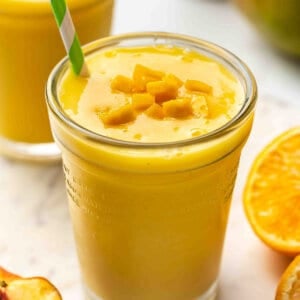 Close-up of a mango orange smoothie in a glass topped with diced mango and a green striped straw.