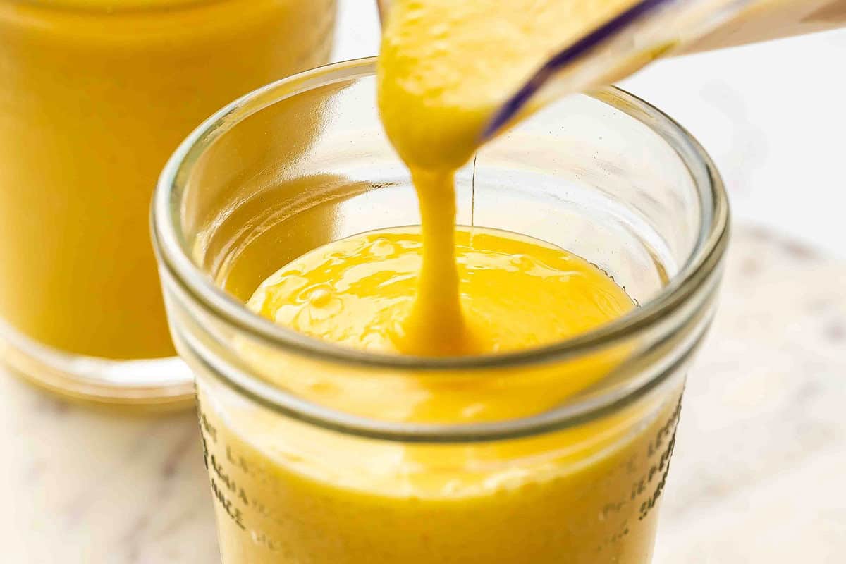 Mango orange smoothie being poured from a blender into a glass jar.