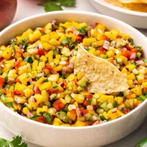 Side view of a bowl of mango salsa with a tortilla chip.