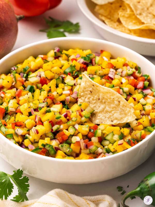 Side view of a bowl of mango salsa with a tortilla chip.