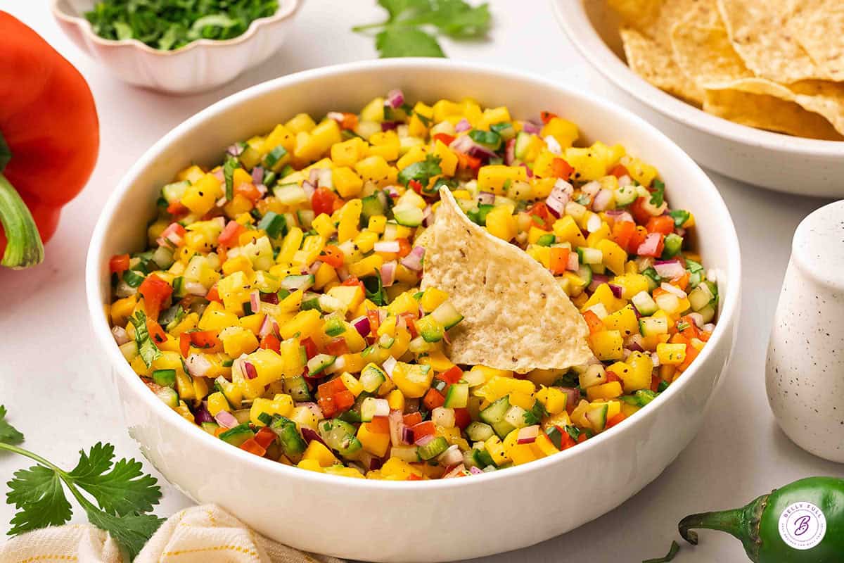Side view of a bowl of fresh mango salsa with a tortilla chip.