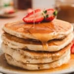 A stack of pancakes topped with maple butter syrup and strawberry halves.