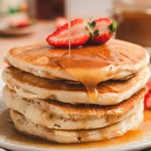 A stack of pancakes topped with maple butter syrup and strawberry halves.