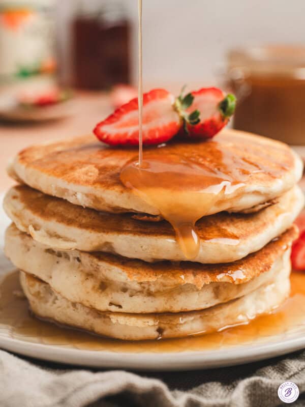 A stack of pancakes topped with maple butter syrup and strawberry halves.
