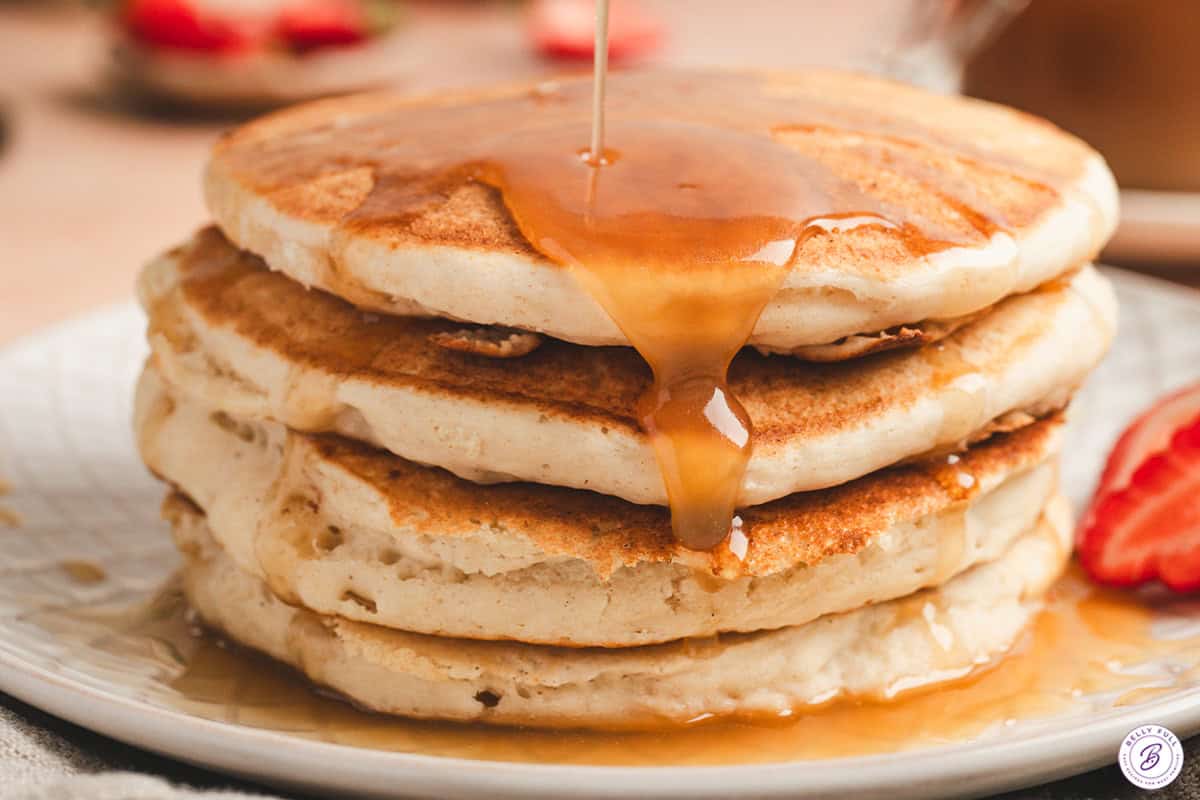 Side view of a stack of pancakes topped with maple butter syrup.