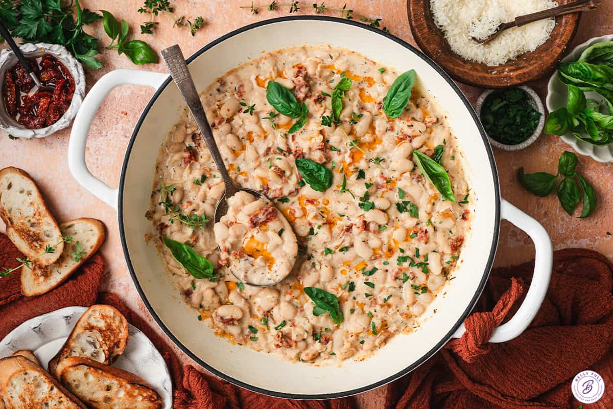 Marry me beans in a skillet with fresh basil and a serving spoon.