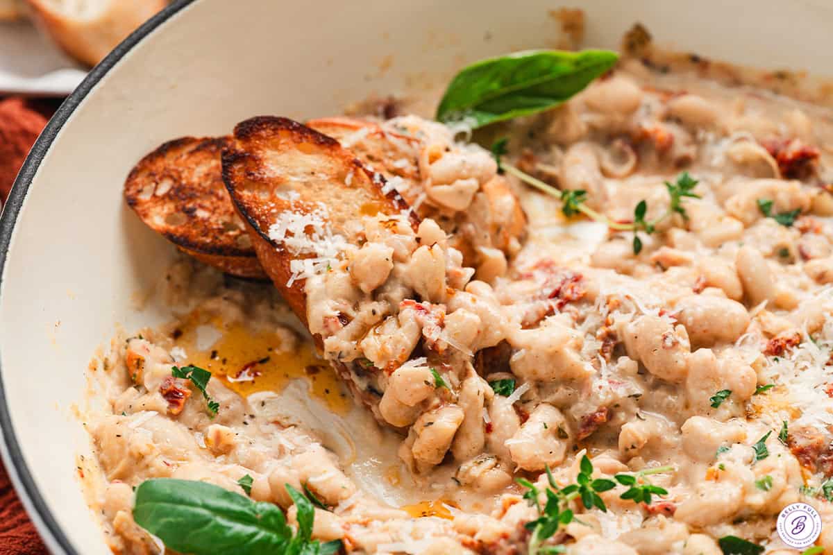 Side view of Marry Me beans in a skillet with slices of crusty bread.