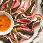 Overhead view of a platter of mini pickle salami tacos with a bowl of hot honey.