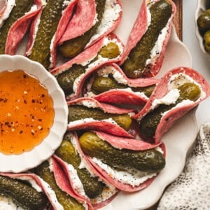 Overhead view of a platter of mini pickle salami tacos with a bowl of hot honey.