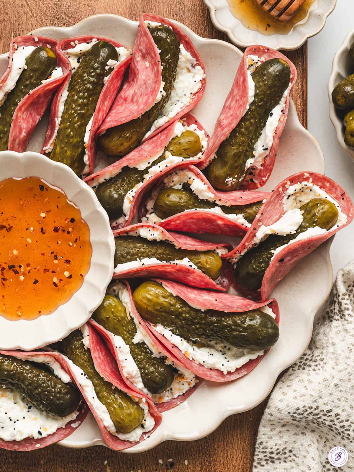 Overhead view of a platter of mini pickle salami tacos with a bowl of hot honey.