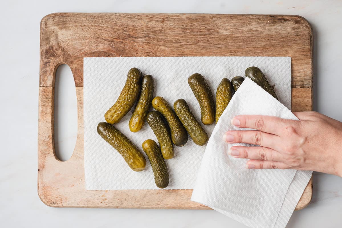 A hand drying mini pickles with paper towels.