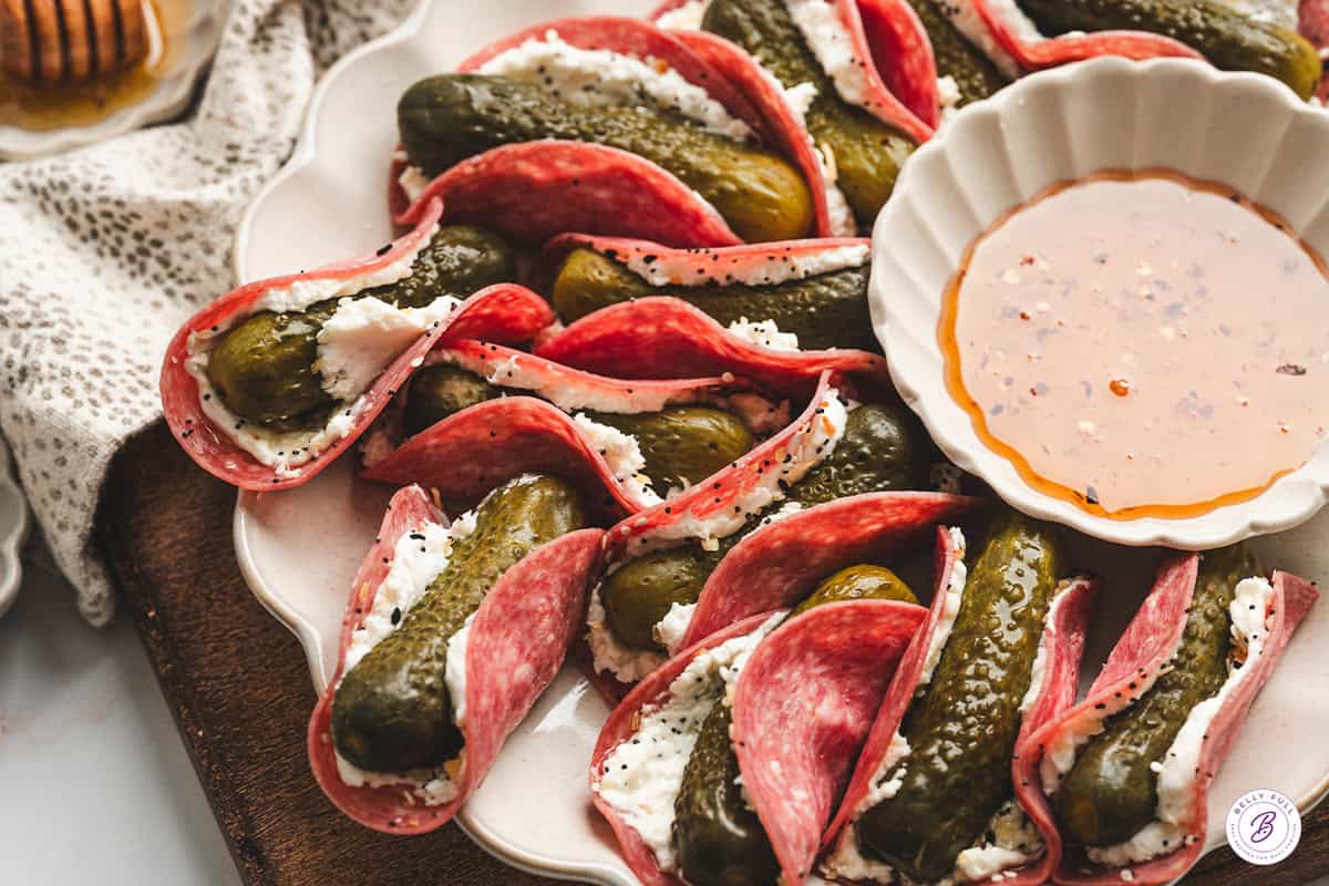 A platter of pickle tacos with a bowl of hot honey.