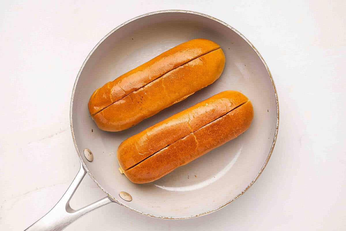 Brioche hot dog rolls toasting in a skillet.