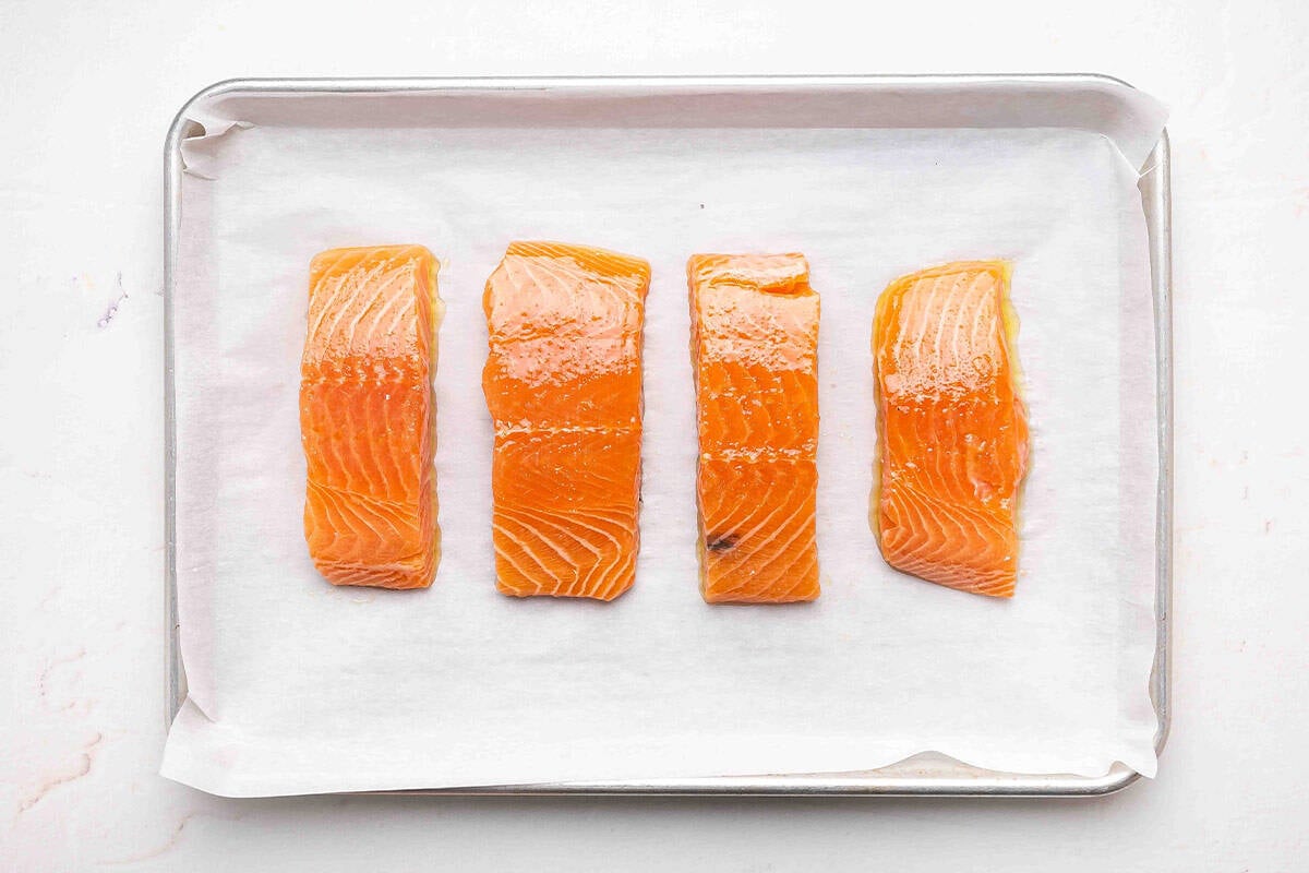 Four salmon filets coated in olive oil on a parchment lined baking sheet.