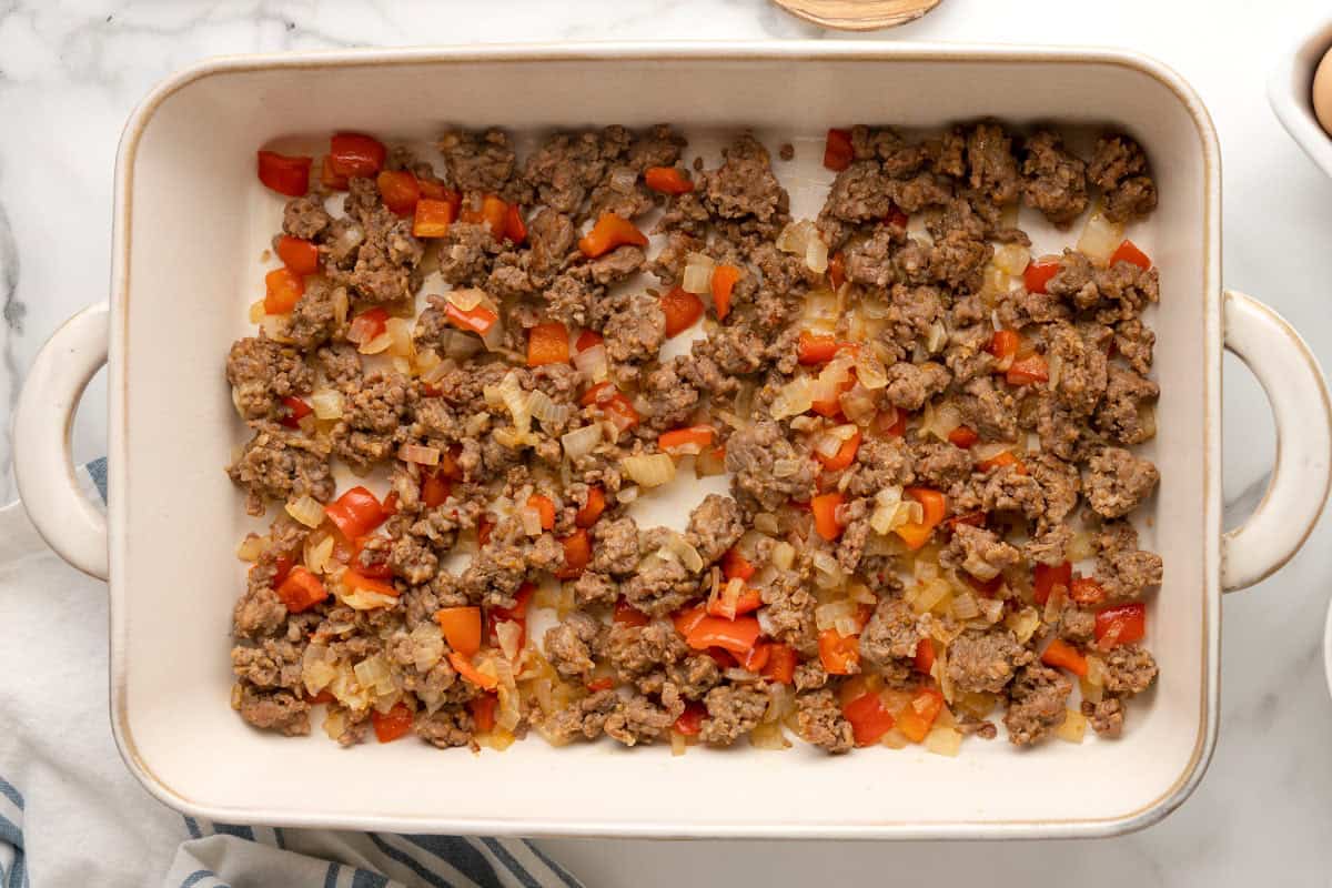 Browned breakfast sausage, onion, and red bell pepper spread in an even layer in a white casserole dish